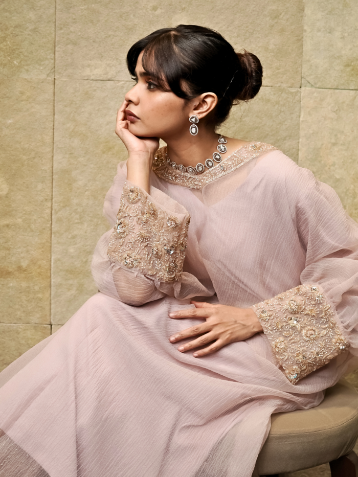 Woman wearing an elegant pastel rose pink embroidered kurta set with flared sleeves and a matching dupatta.