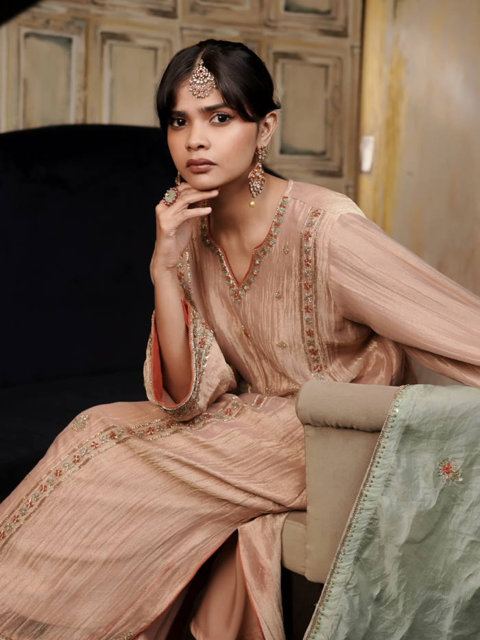 Woman wearing a pastel peach embroidered silk kurta set with a contrasting sage green organza dupatta.